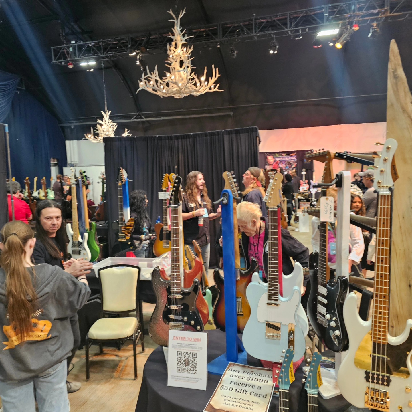 Packed LVGTS show floor — guitars on display under the Veil Pavilion's antler chandeliers