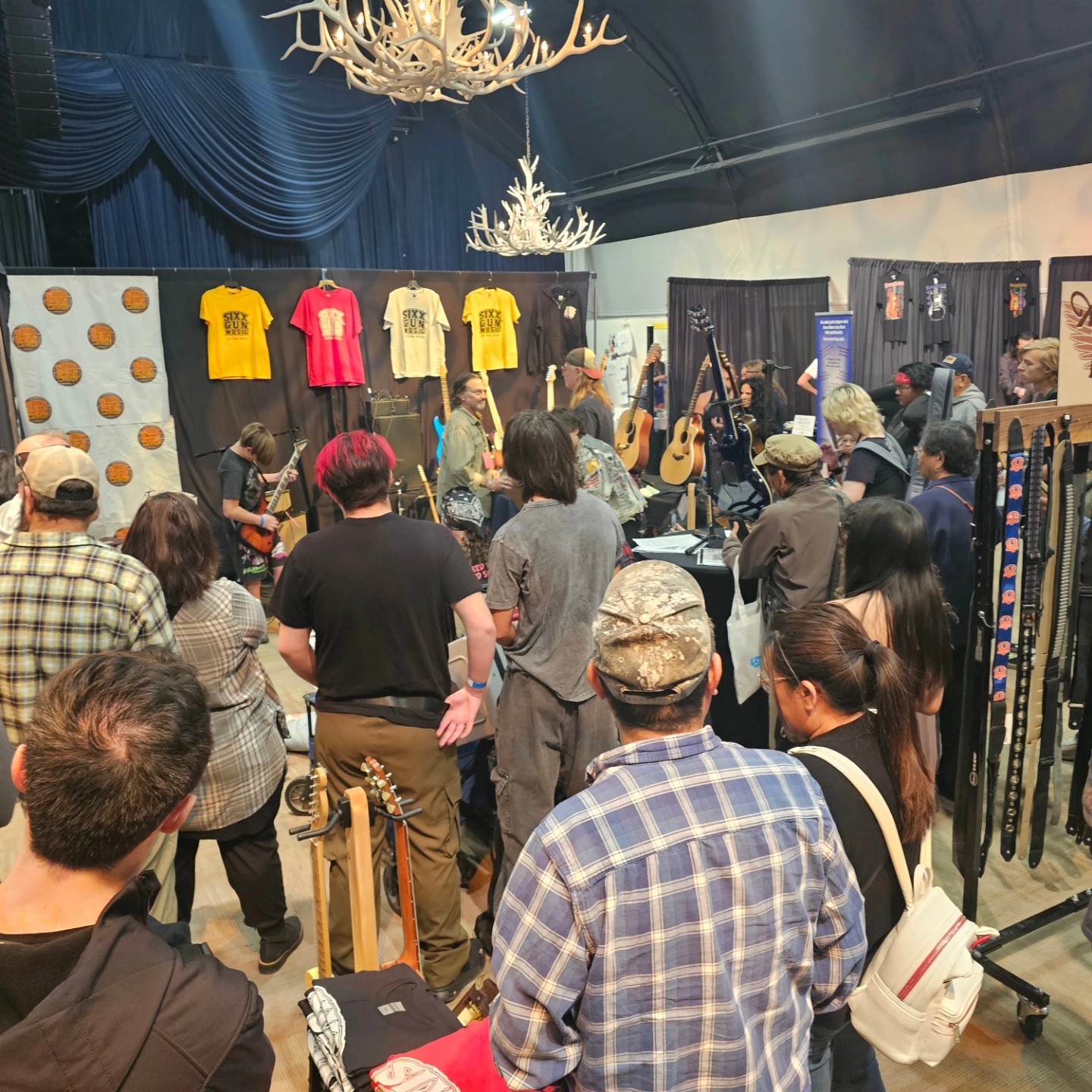 Live performance and crowd at an LVGTS exhibitor booth featuring Sixx Gun Music merch